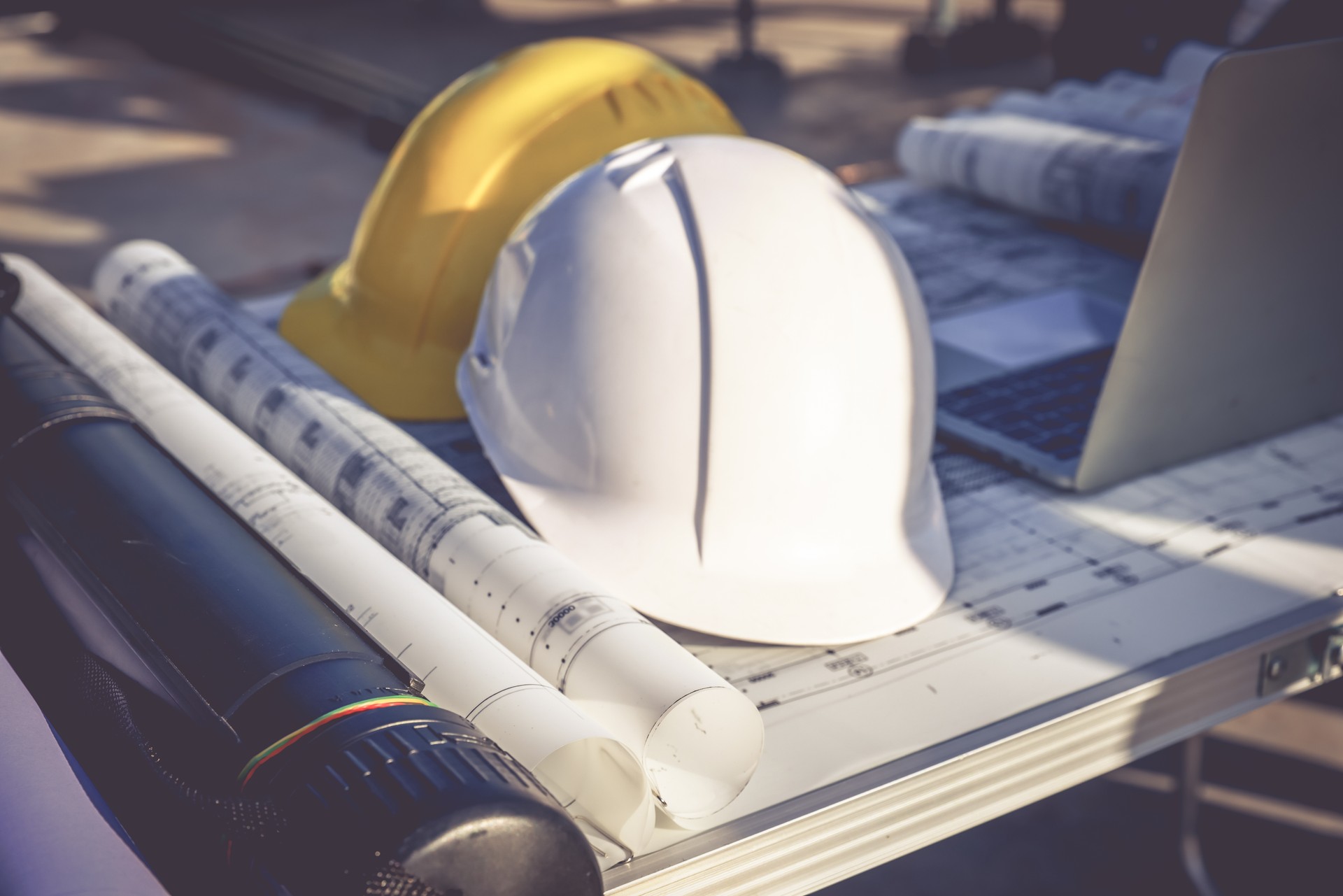 Close up Safety Helmet , blue print drawing and laptop on table at construction sideline , Engineering and Investment concept